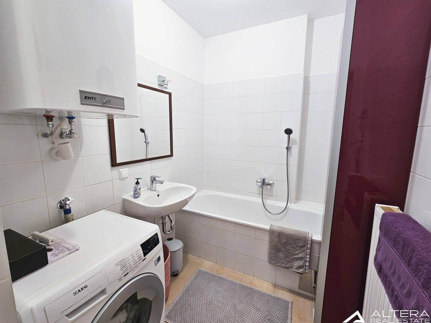 Badezimmer mit Badewanne, Waschbecken, Waschmaschine und weißen Wandfliesen.