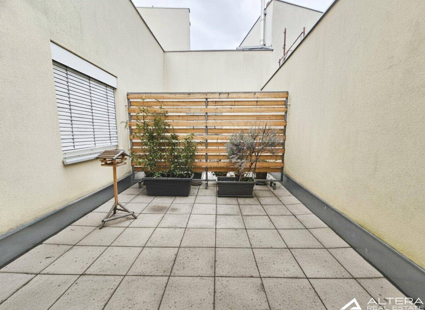 Helle Außenterrasse mit Fliesenboden und Sichtschutz, ideal für entspannte Stunden.