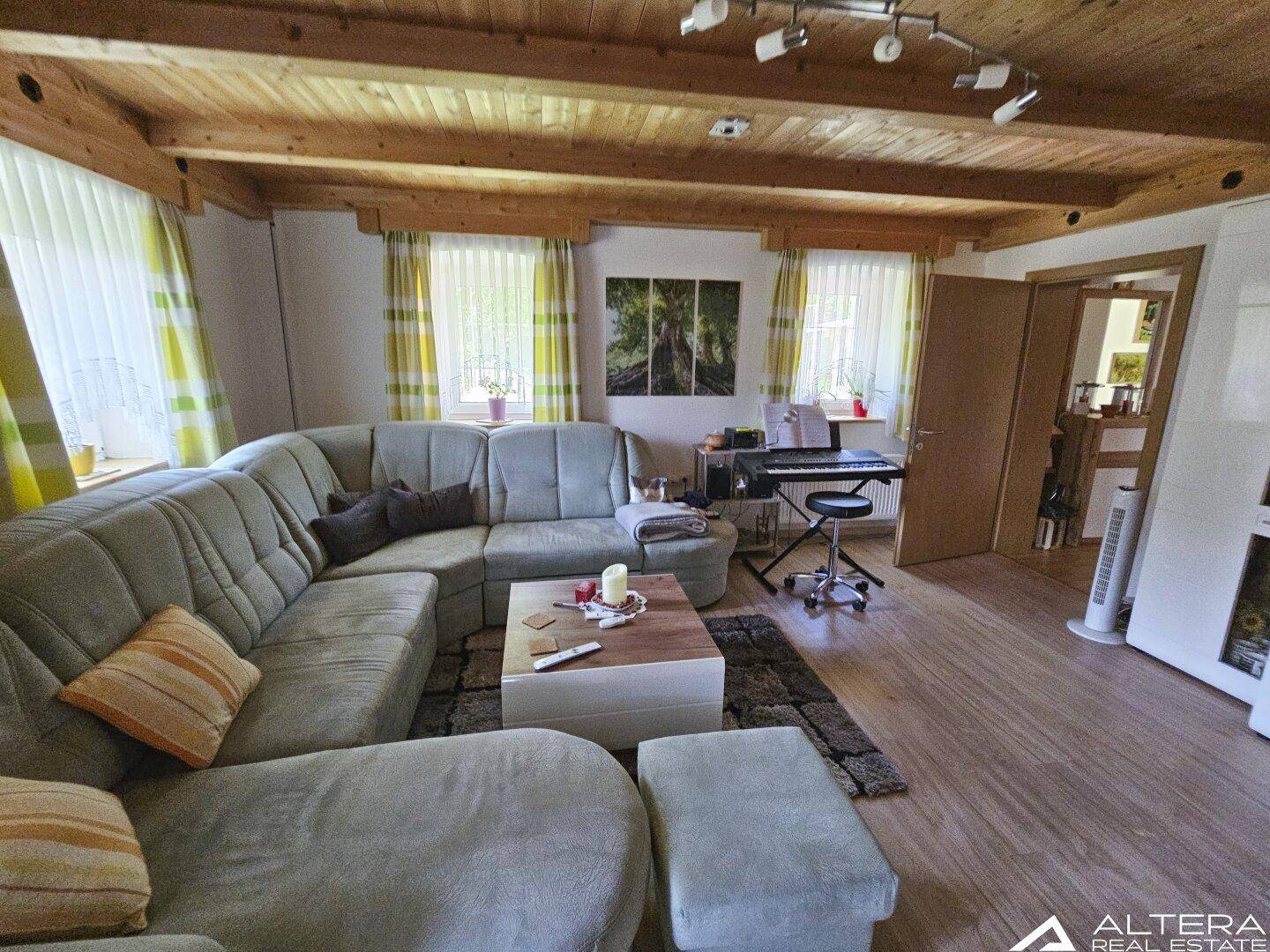 Gemütliches Wohnzimmer mit großer Eckcouch, Holzbalkendecke und Laminatboden.