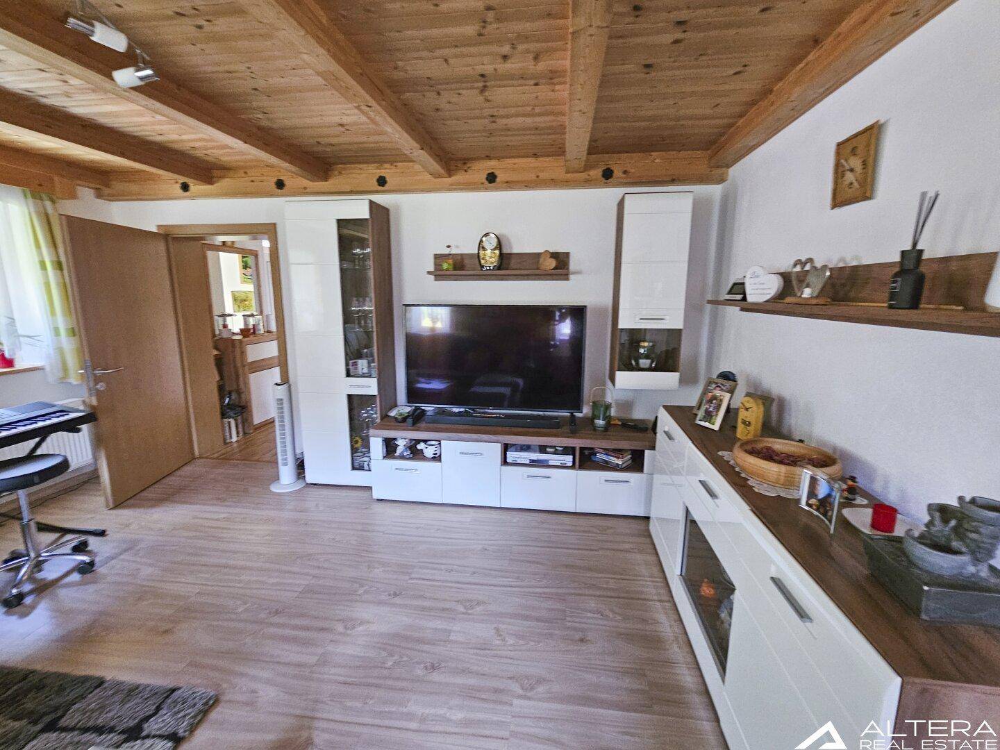 Wohnzimmer mit moderner TV-Wand, Holzbalkendecke und Laminatboden, hell und einladend.