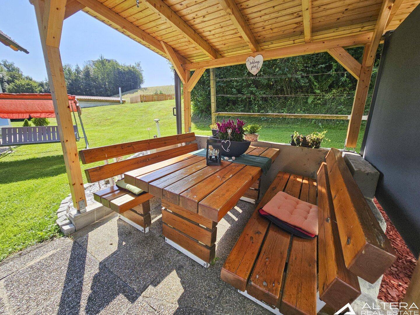 Überdachte Terrasse mit rustikalen Holzmöbeln und Blick ins Grüne, ideal für Mahlzeiten im Freien.