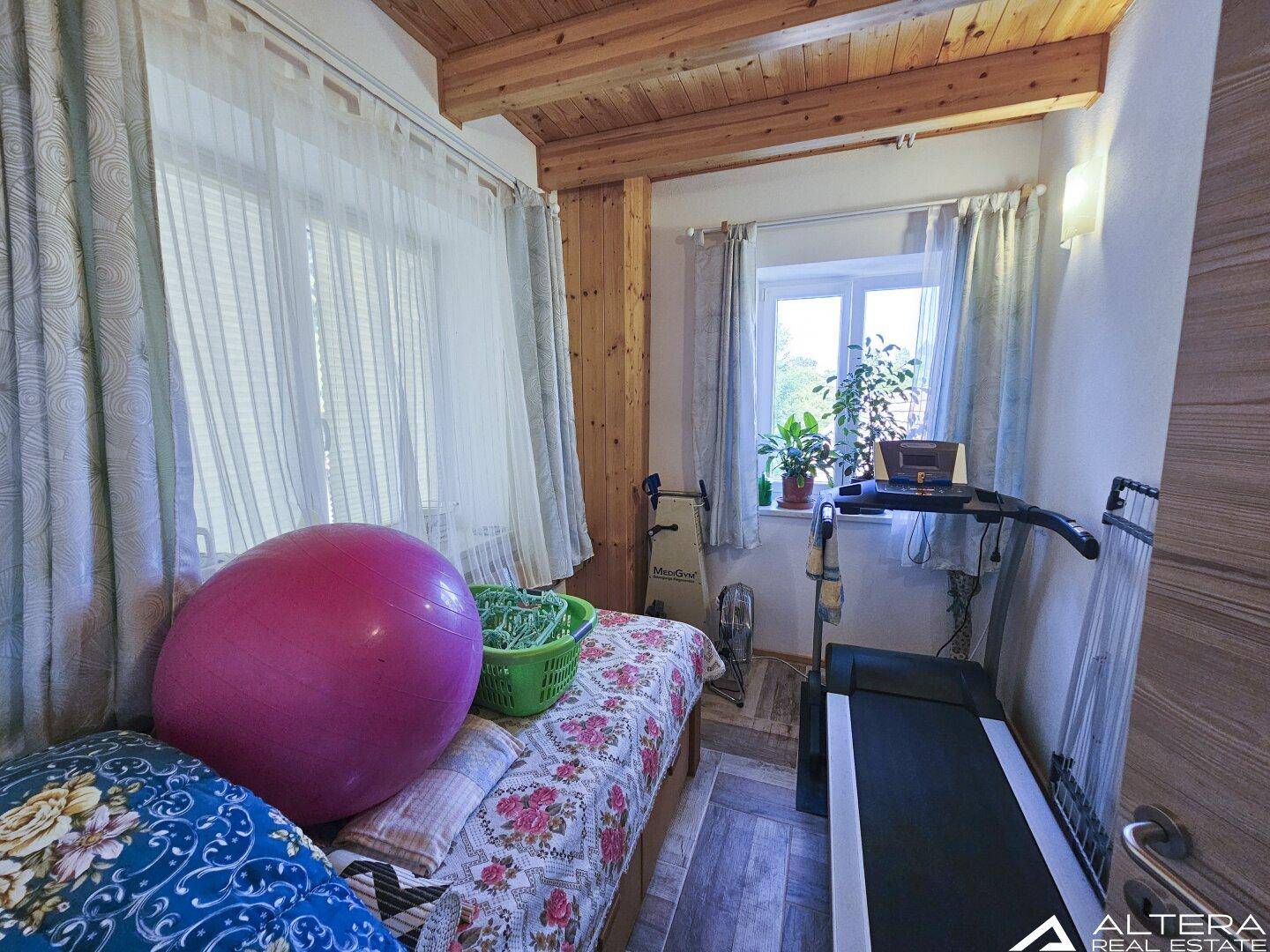 Kleines Arbeitszimmer mit Laufband, Holzbalken und Fenster, ideal für Home-Office oder Sport.