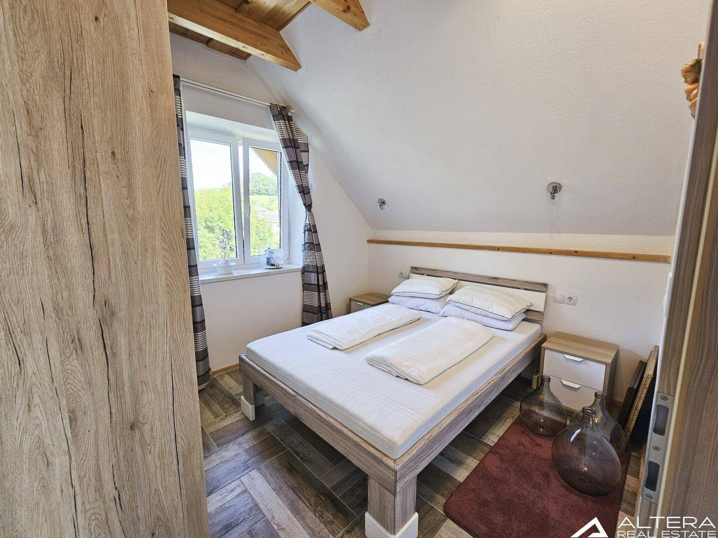 Schlafzimmer im Dachgeschoss mit Holzbalkendecke, Doppelbett und schrägen Wänden.