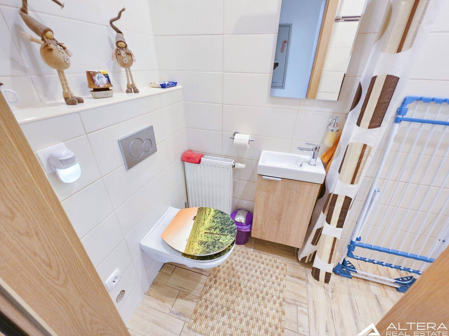Separate Toilette mit Wand-WC, Einzelwaschbecken und hellen Fliesen, praktisch und gepflegt.