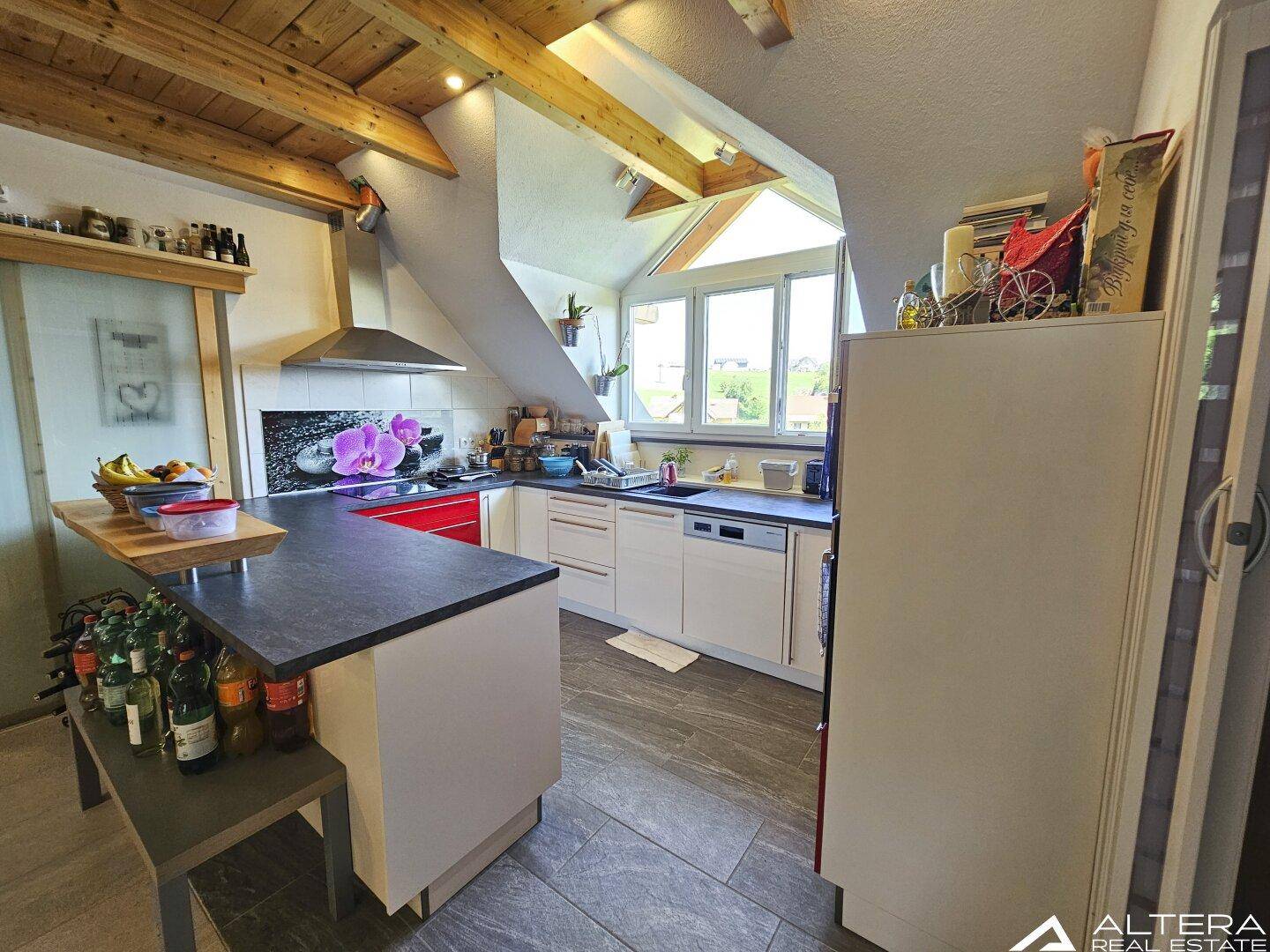 Moderne Küche im Dachgeschoss mit Einbaugeräten, dunkler Arbeitsplatte und Holzbalkendecke.