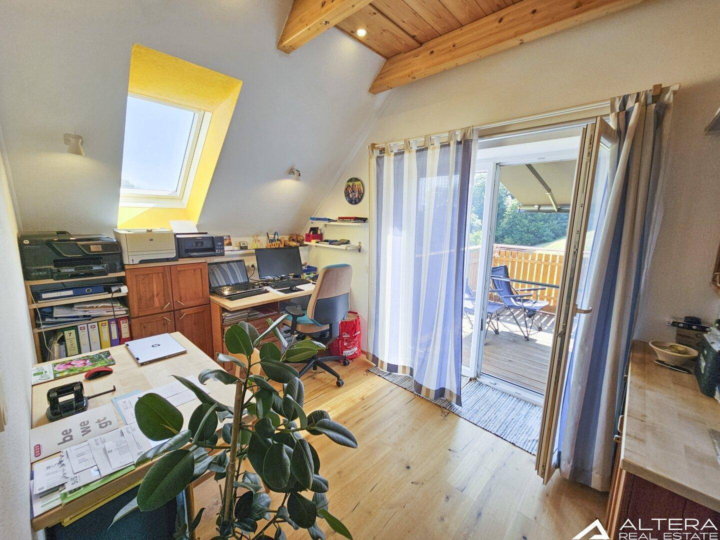 Helles Arbeitszimmer mit Schreibtisch, Dachfenster und Zugang zum Balkon, mit Holzboden.