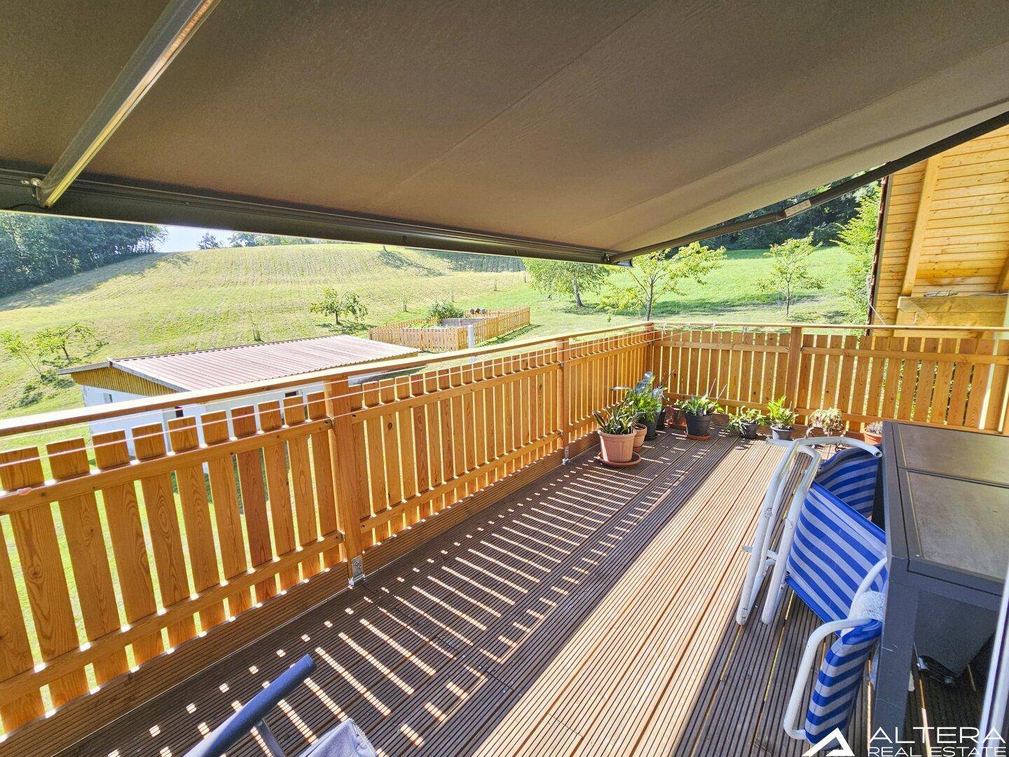 Geräumiger Holzbalkon mit Markise und Sitzgelegenheiten, bietet weiten Blick ins Grüne.