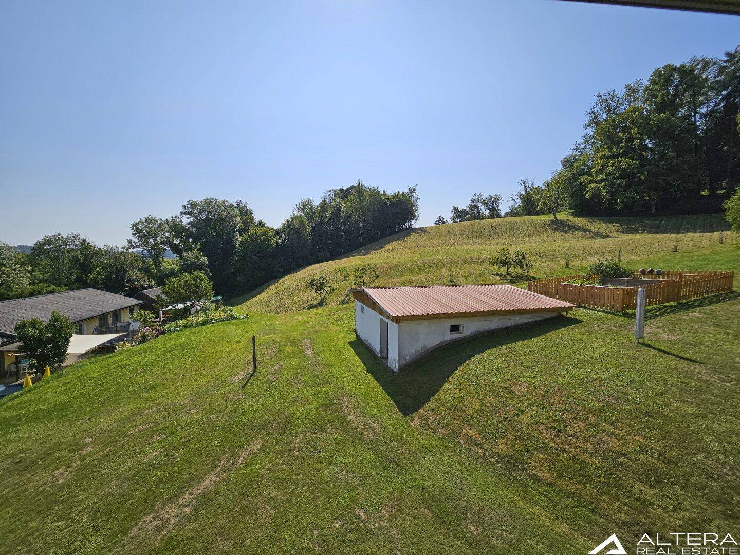Weitläufige grüne Landschaft mit einem kleinen Nebengebäude unter blauem Himmel.