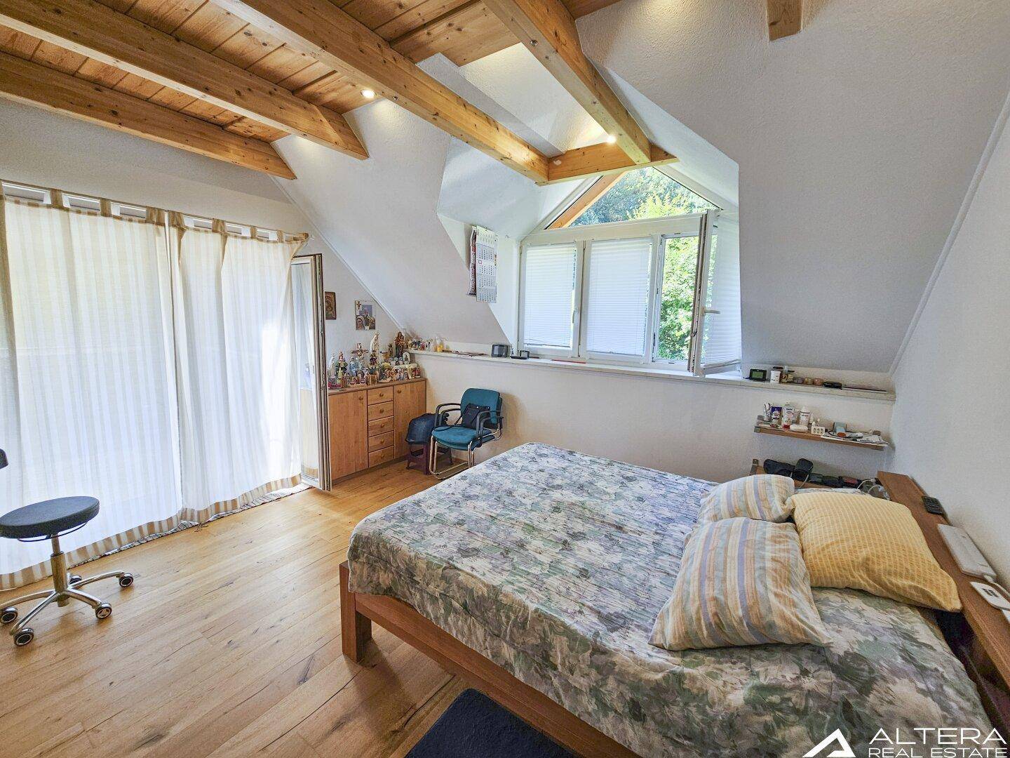 Großes Schlafzimmer im Dachgeschoss mit Holzbalken, Holzboden und großen Fenstern.
