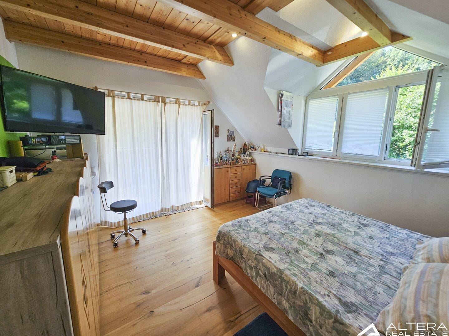 Geräumiges Schlafzimmer mit Holzbalken, TV und Holzboden, hell und komfortabel.