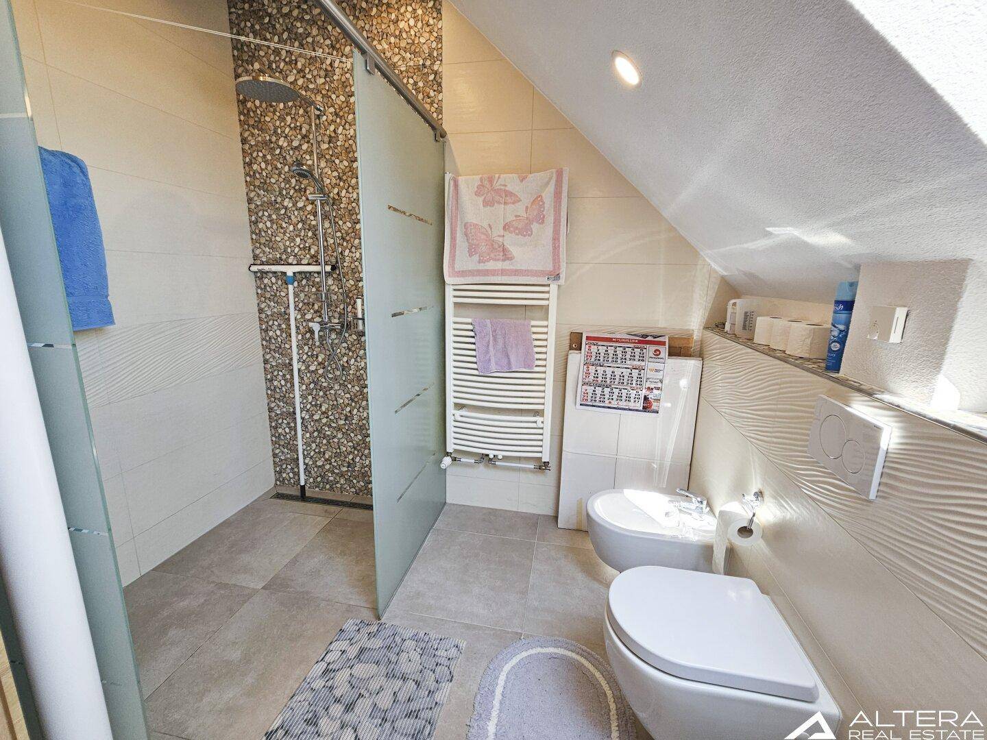 Modernes Badezimmer im Dachgeschoss mit begehbarer Dusche, zwei Toiletten und Handtuchheizkörper.