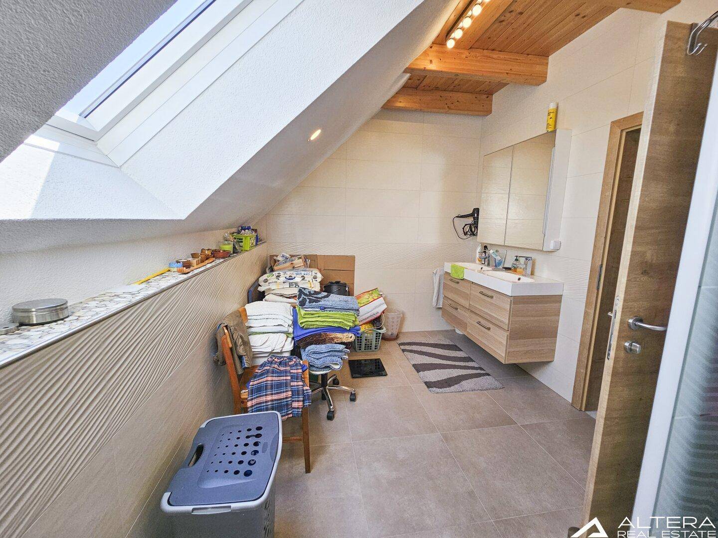 Helles Badezimmer im Dachgeschoss mit Dachfenster, modernem Waschtisch und schrägen Wänden.