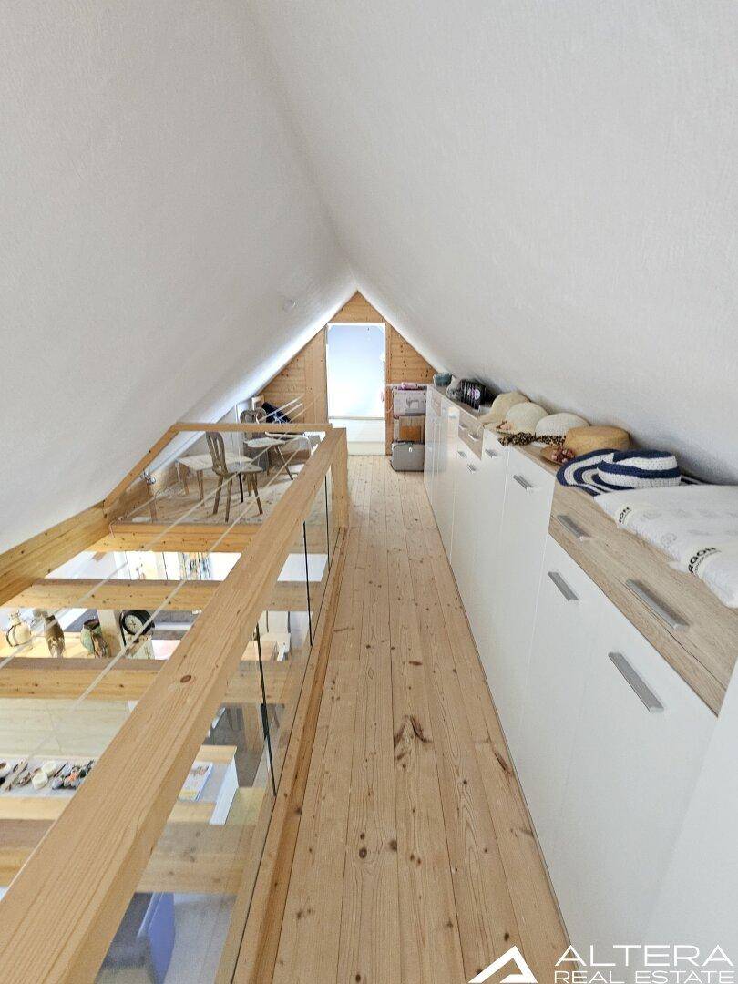 Dachgeschoss-Flur mit Holzboden, sichtbaren Holzbalken und Glasgeländer mit Blick nach unten.