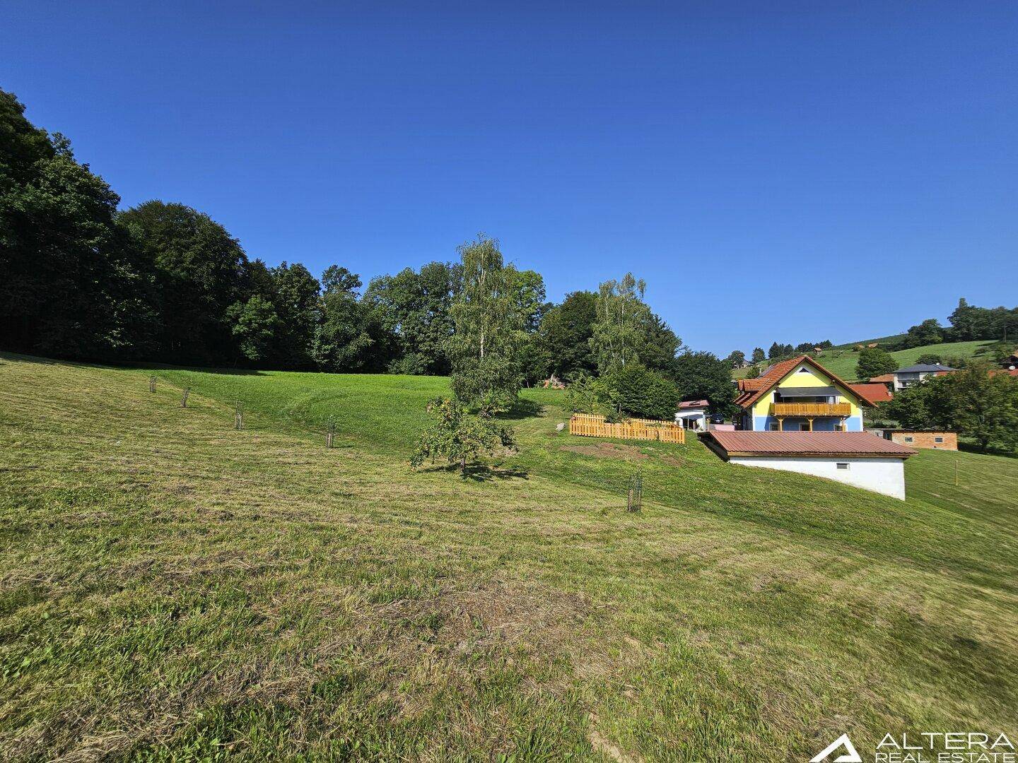 Weitläufige grüne Hügellandschaft mit einem Haus im Hintergrund unter blauem Himmel.