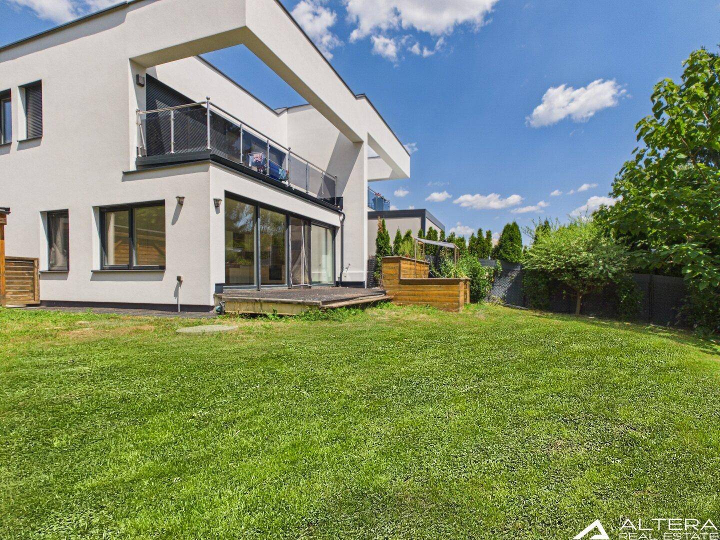 Sonnige Ansicht der modernen Villa mit Balkon, großen Glasfronten und weitläufigem grünen Rasen.