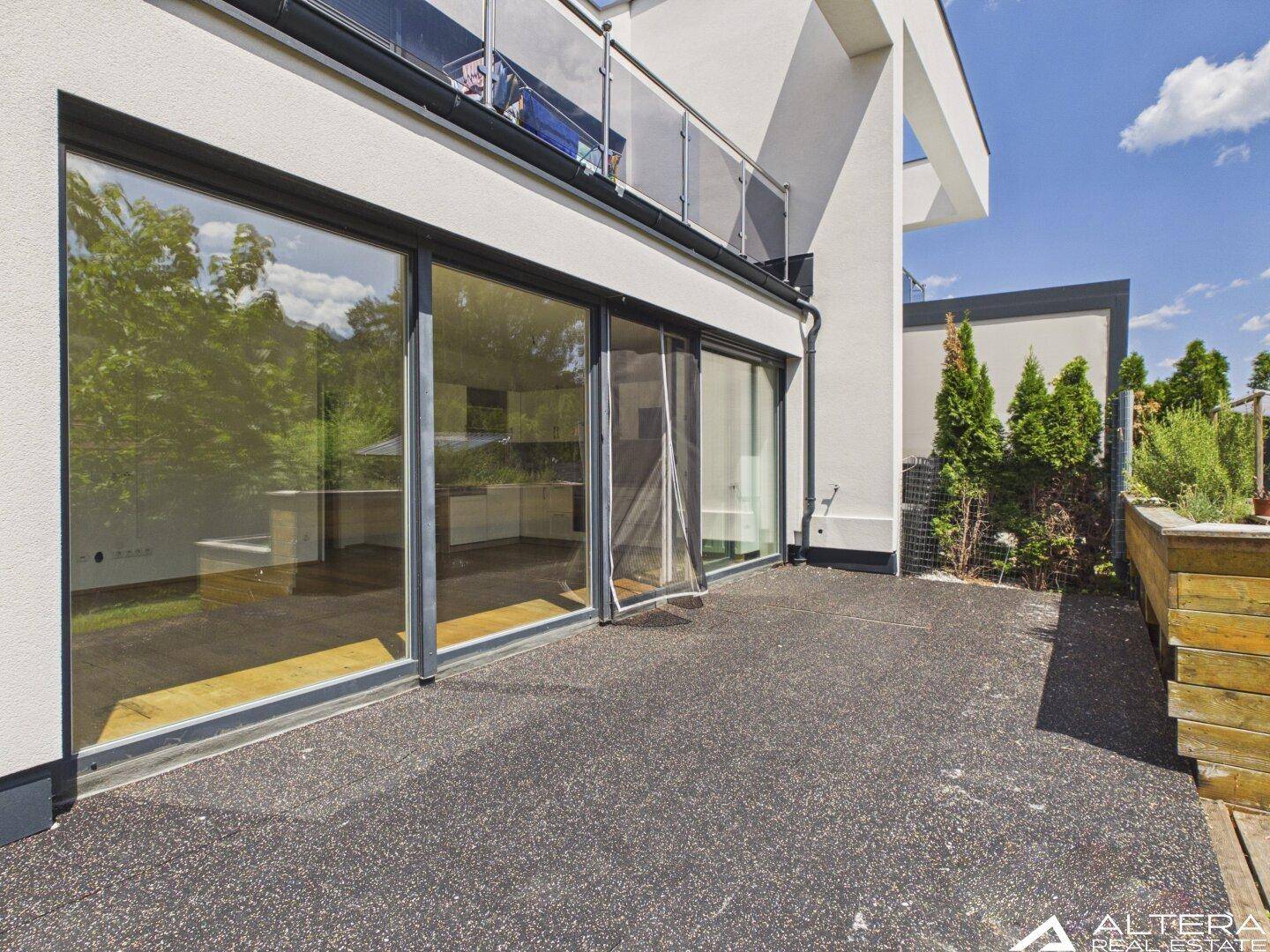 Ebenerdige Terrasse mit dunklem Bodenbelag und großen Glasschiebetüren, die zum Innenbereich führen.