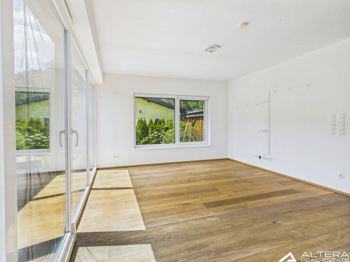 Helles Zimmer mit Holzboden und großem Fenster, das viel Tageslicht hereinlässt.