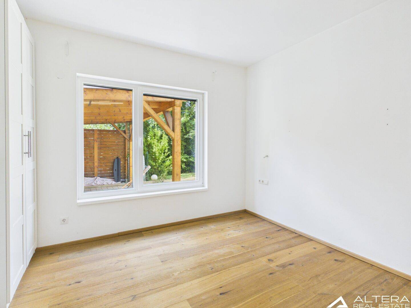 Helles Schlafzimmer mit Holzboden und Fenster, das einen Blick auf eine Holzkonstruktion im Freien bietet.