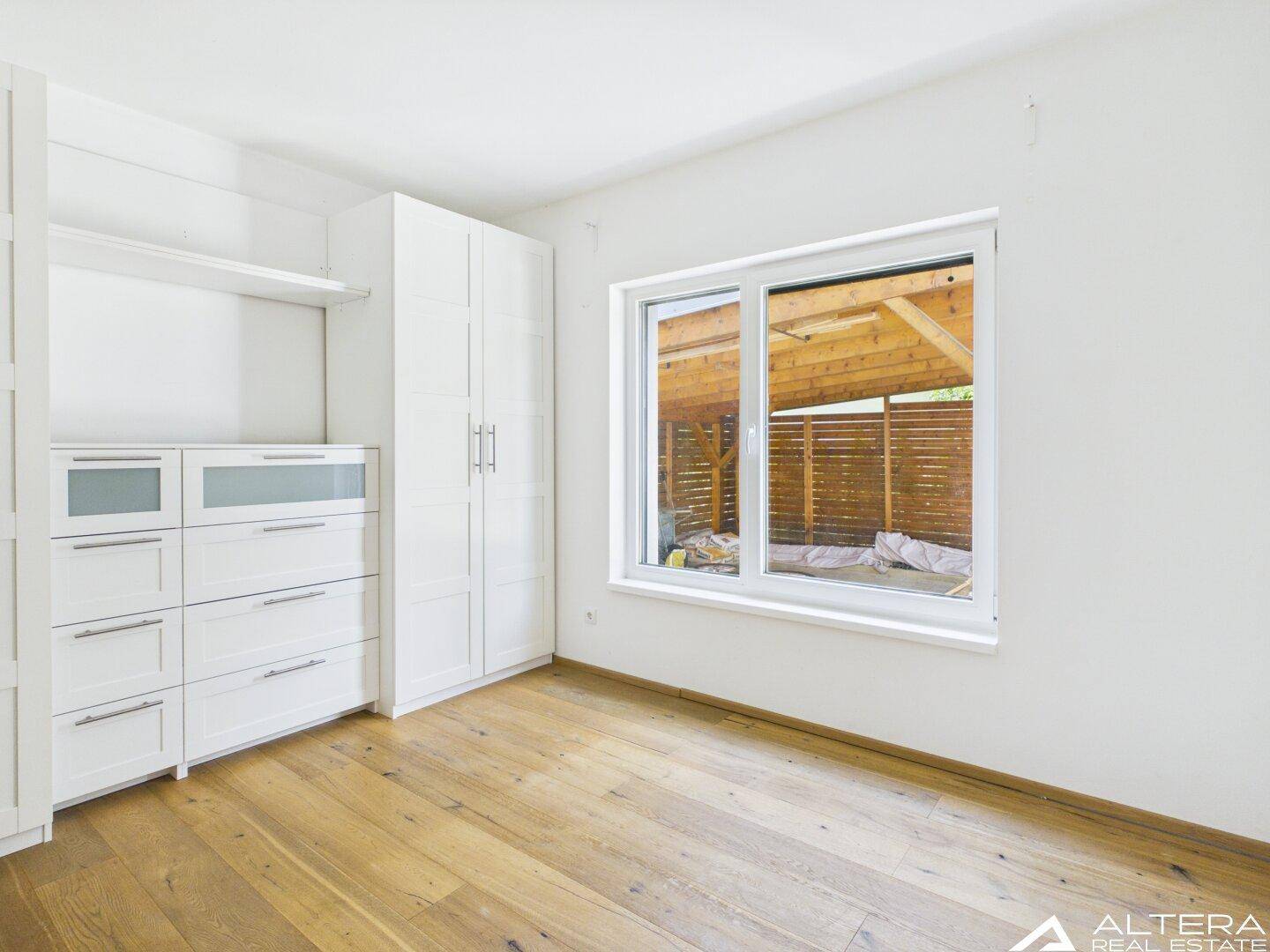 Schlafzimmer mit Holzboden, Fenster und praktischen weißen Einbauschränken und Kommoden.