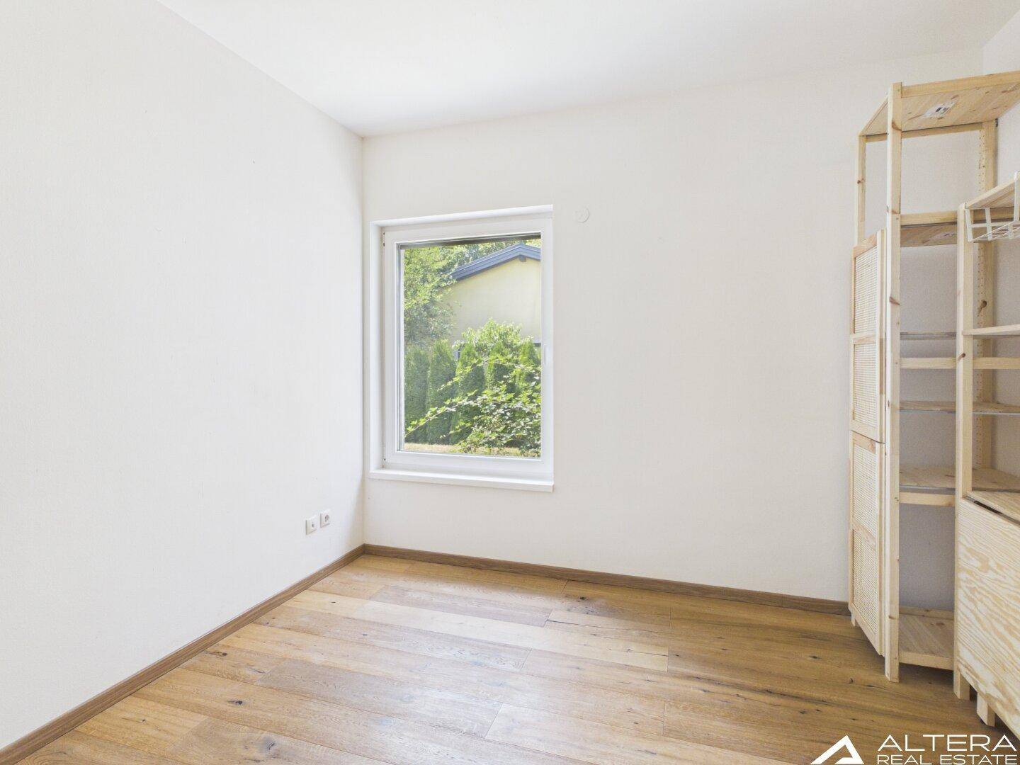 Helles Zimmer mit Holzboden und Fenster, ausgestattet mit einem einfachen Holzregalsystem.