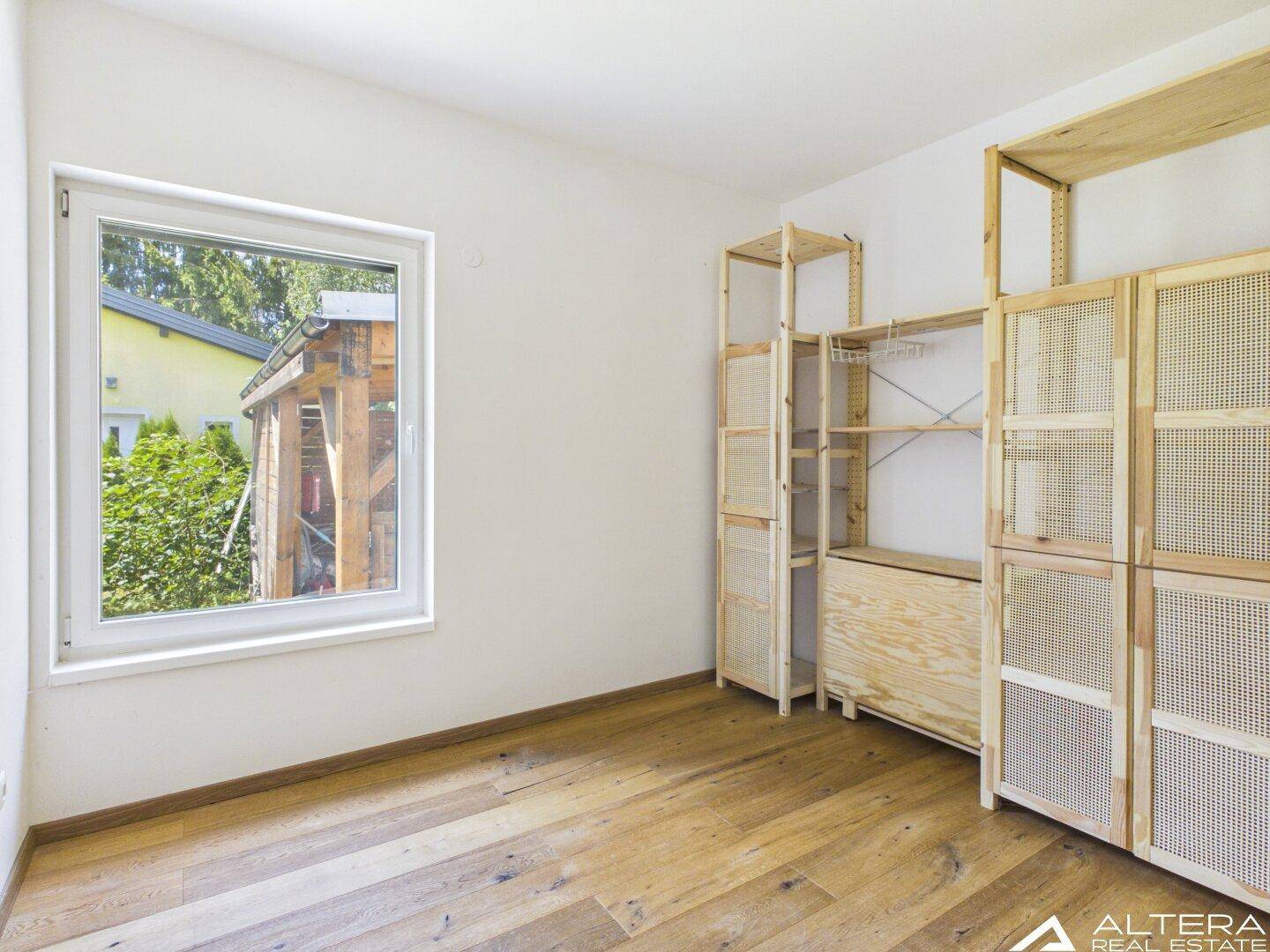 Schlafzimmer mit Holzboden, Fenster und praktischen Holzregalen für Stauraum.