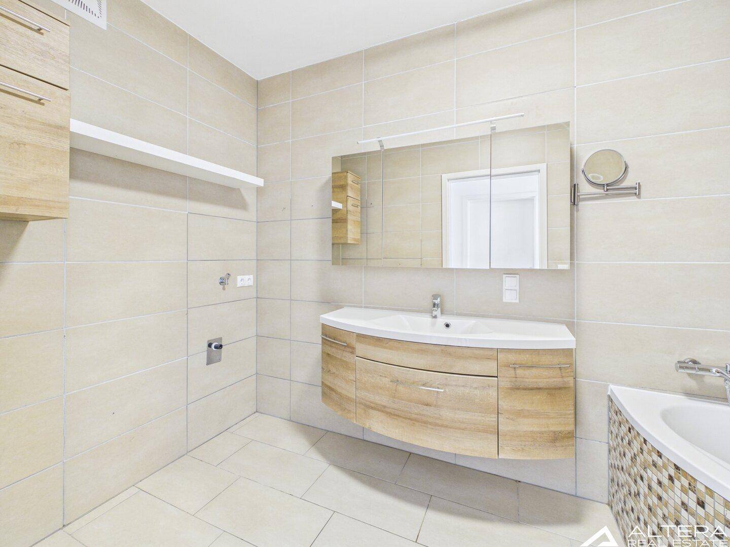 Modernes Badezimmer mit beigefarbenen Fliesen, Holzwaschtisch, großem Spiegelschrank und Eckbadewanne.