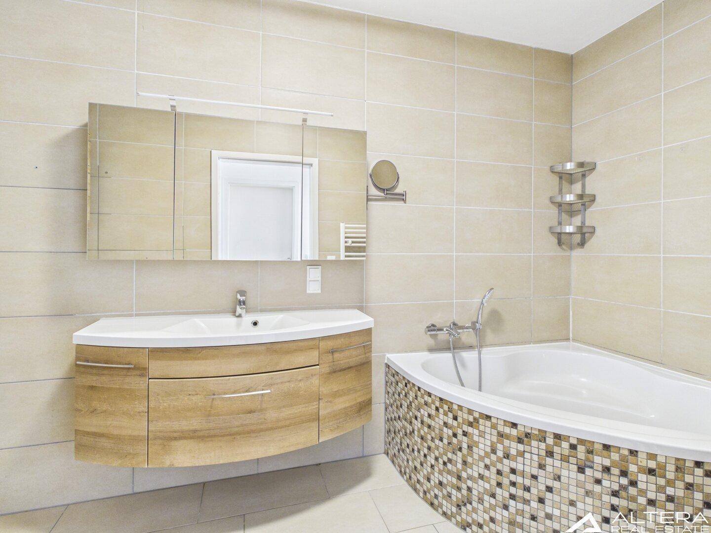 Elegantes Badezimmer mit beigefarbenen Fliesen, modernem Waschtisch und einer stilvollen Eckbadewanne.