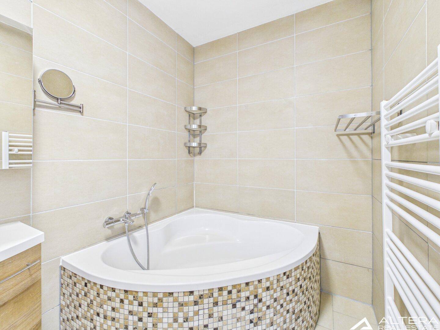Detailansicht der Eckbadewanne mit Mosaikfliesen und einem praktischen beheizten Handtuchhalter.