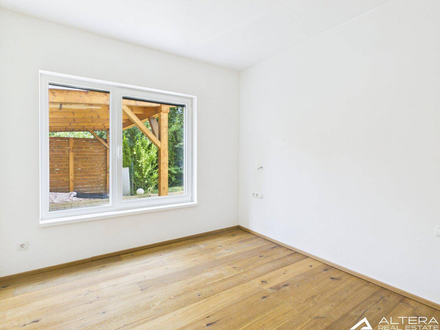 Helles Schlafzimmer mit Holzboden und Fenster, das einen Blick auf eine Holzkonstruktion im Freien bietet.