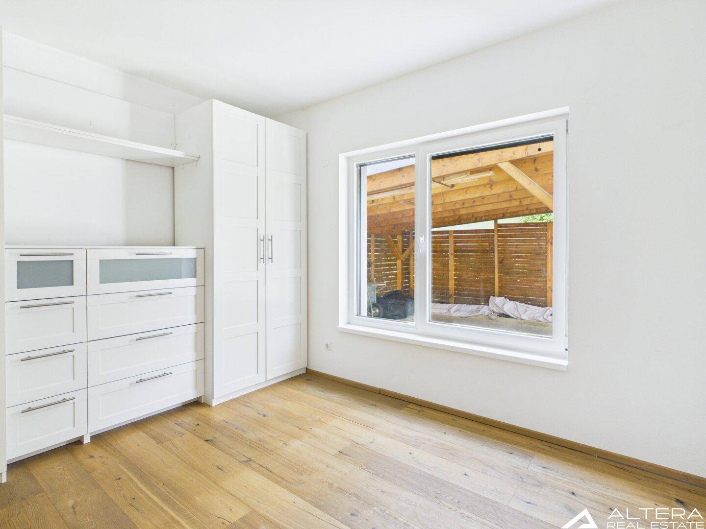 Schlafzimmer mit Holzboden, Fenster und praktischen weißen Einbauschränken und Kommoden.