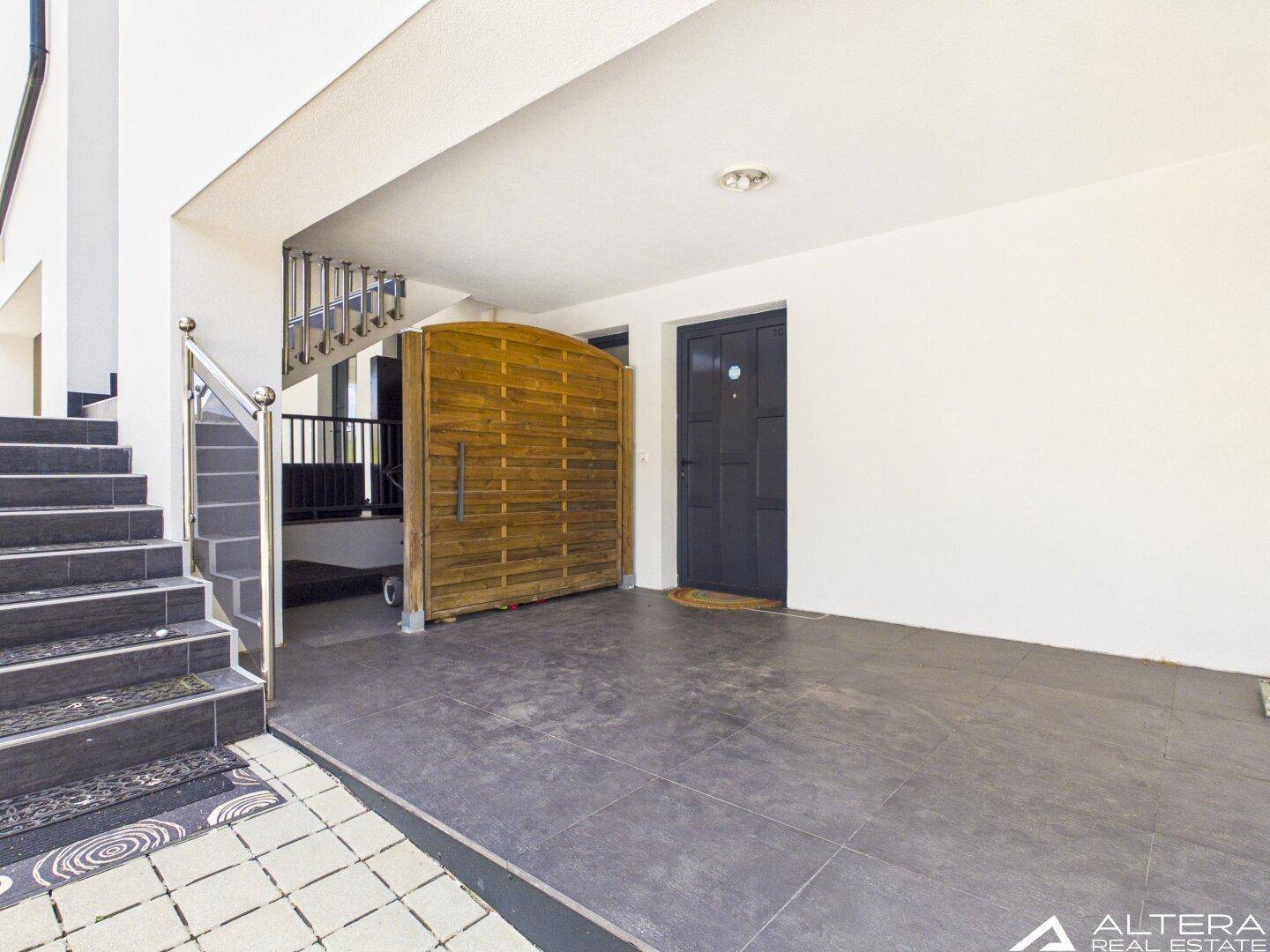 Heller Eingangsbereich mit Treppe, dunkler Tür und Holztor, das zu einem weiteren Bereich führt.