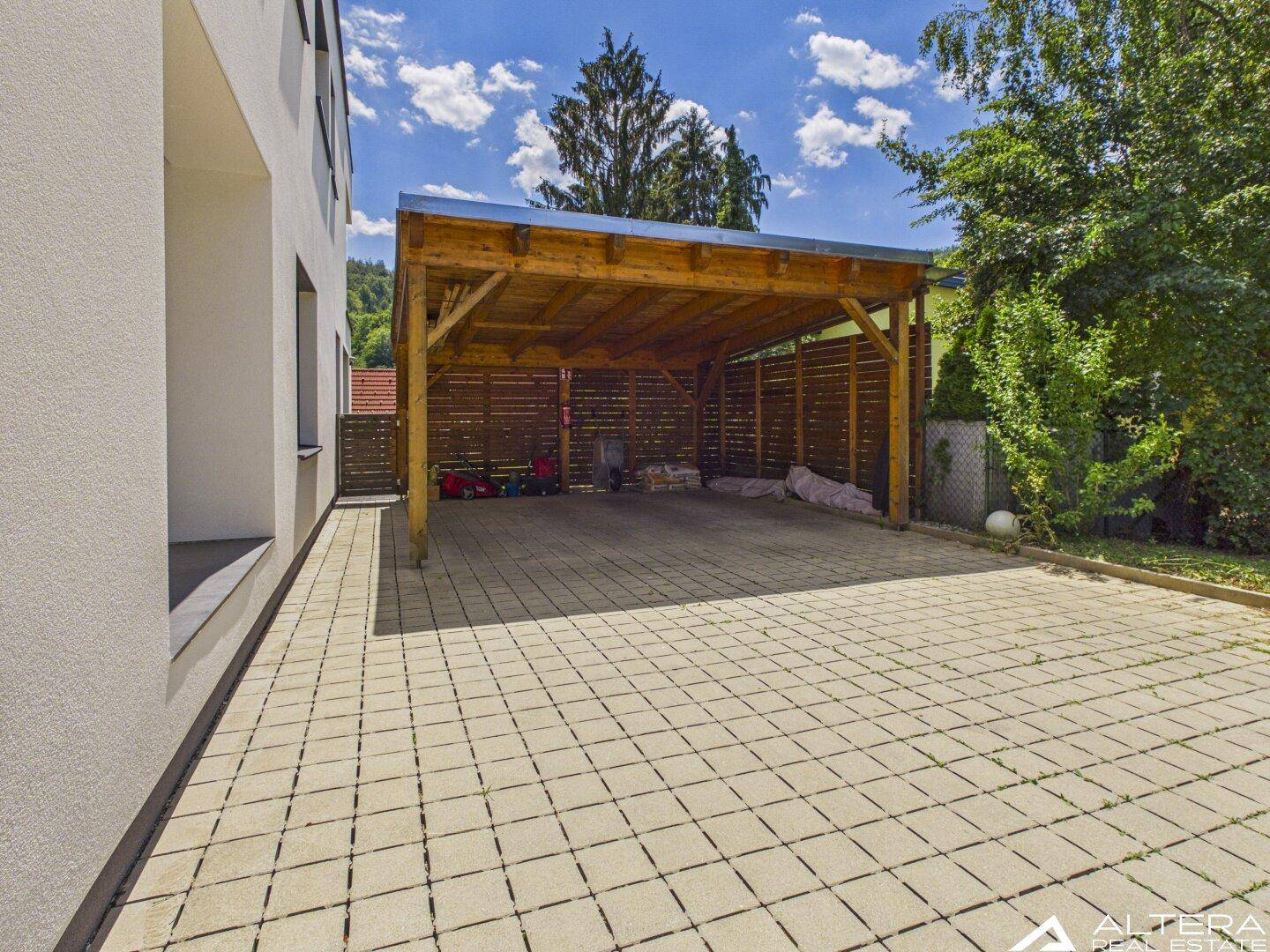 Überdachter Carport aus Holz mit gepflastertem Boden und Stauraum im Freien.