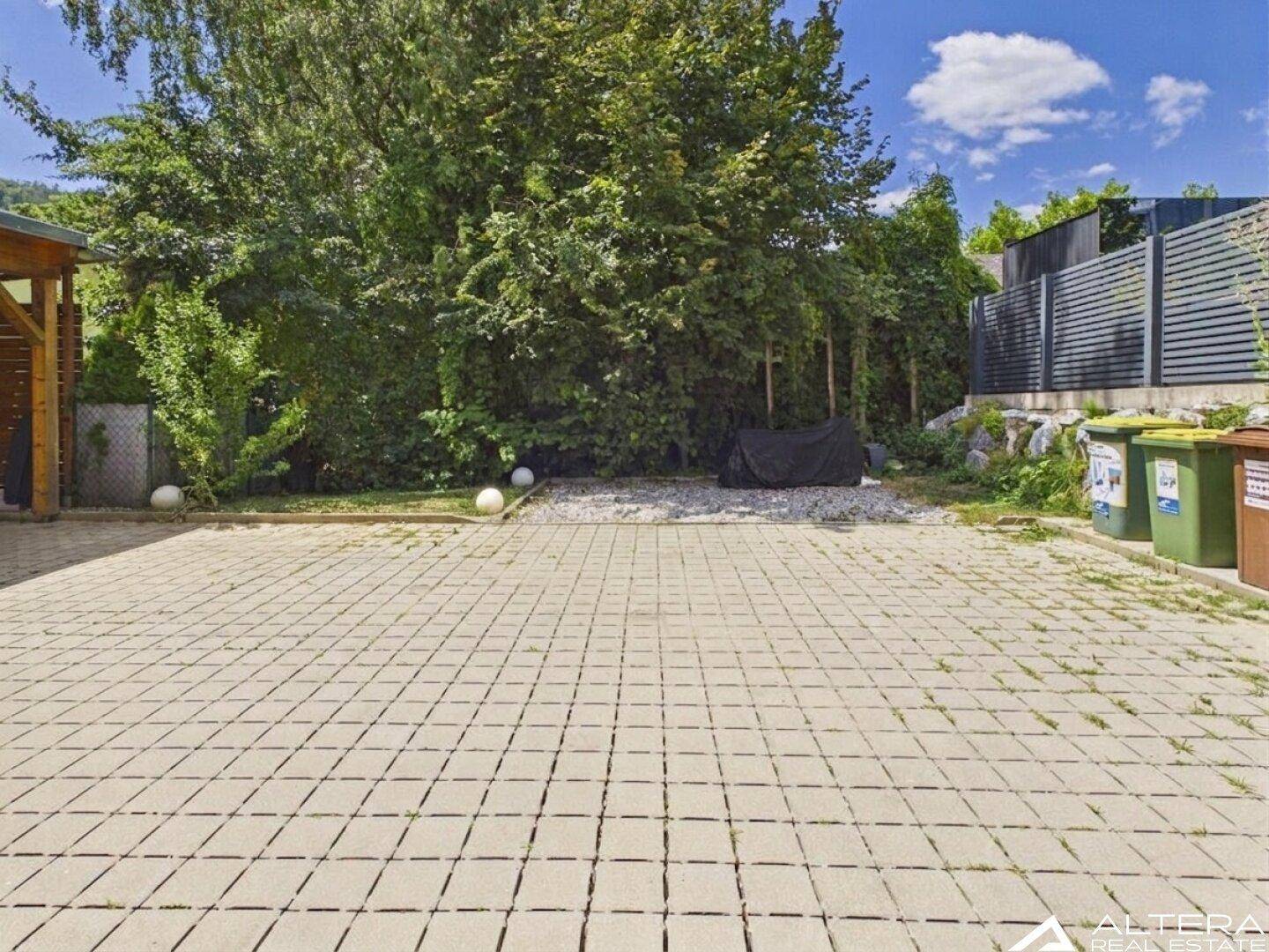 Große gepflasterte Außenfläche mit viel Grün und Bäumen im Hintergrund, ideal für Parkplätze.