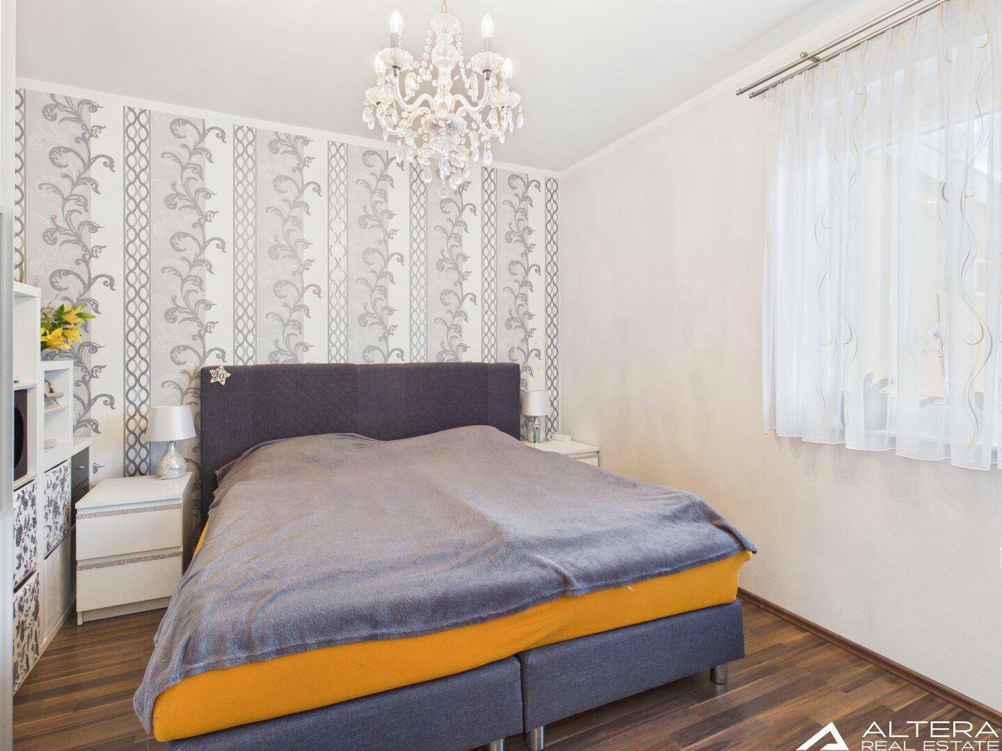 Gemütliches Schlafzimmer mit großem Bett, eleganter Tapete und Kronleuchter, bietet eine ruhige Atmosphäre.
