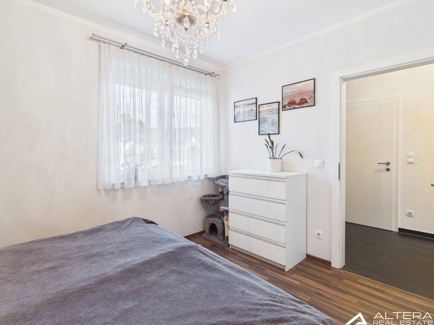 Helles Schlafzimmer mit Fenster, Kommode und schlichtem Dekor, ideal für erholsame Nächte.