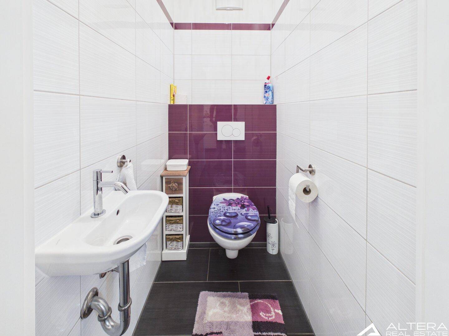 Separates Gäste-WC mit wandhängendem WC und kleinem Waschbecken, modern gefliest und sauber.