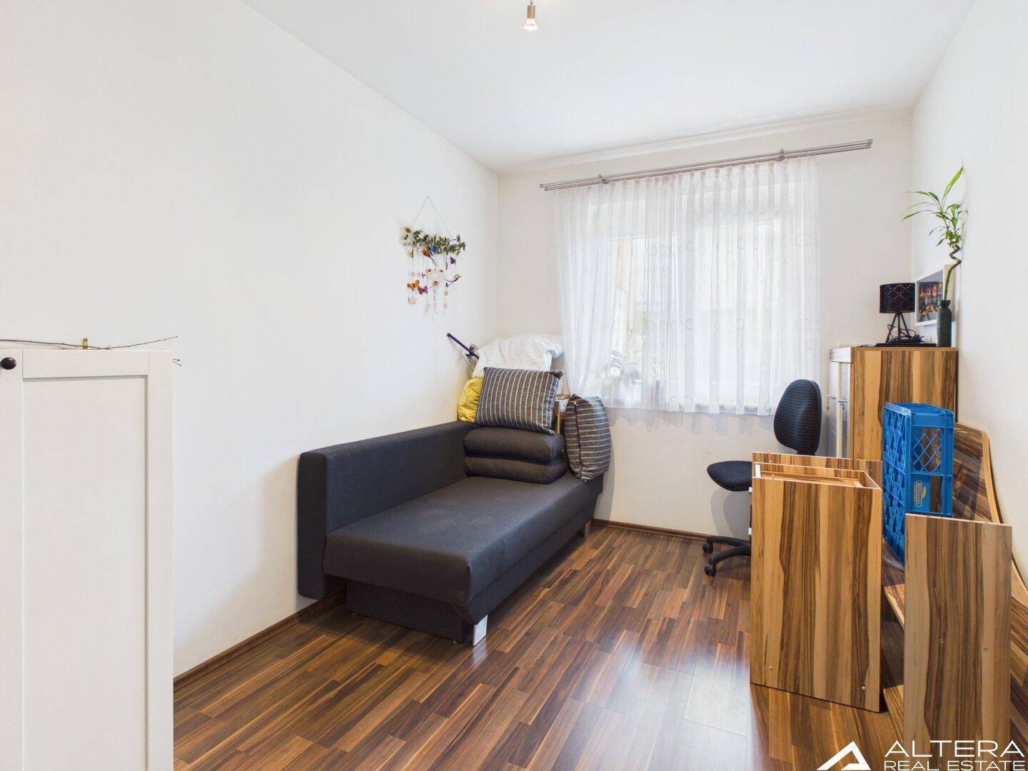 Vielseitiges Zimmer mit Schlafsofa und Holzfußboden, ideal als Gästezimmer oder Arbeitsbereich nutzbar.