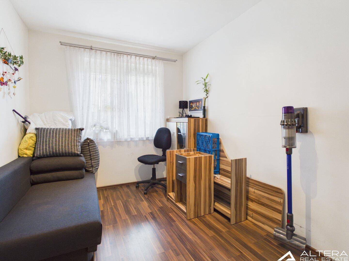 Helles Zimmer mit Holzfußboden und Fenster, bietet flexible Nutzungsmöglichkeiten für Bewohner.
