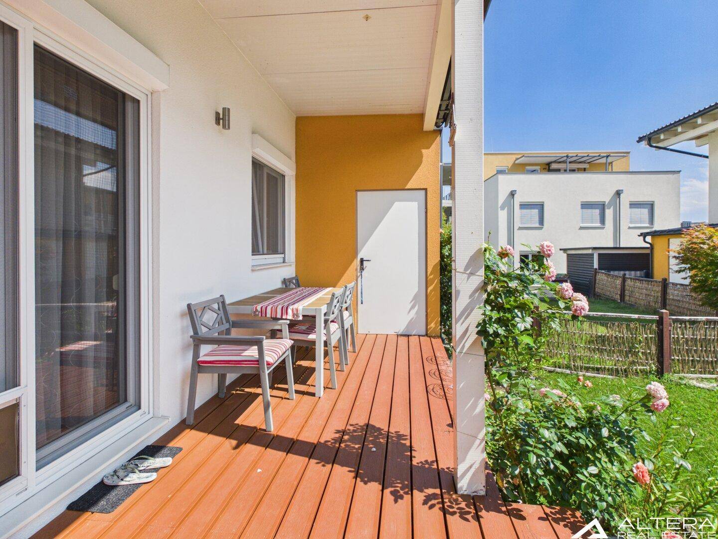 Überdachte Holzterrasse mit Esstisch und Stühlen, perfekt für Mahlzeiten im Freien an sonnigen Tagen.