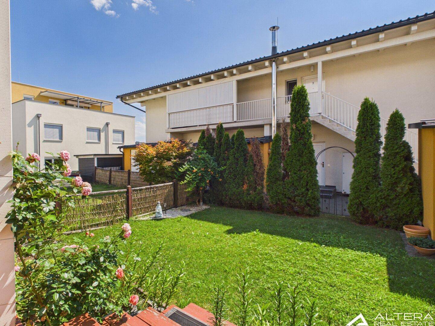 Rückansicht des Hauses mit großem Garten, externer Treppe und gepflegter Grünfläche.