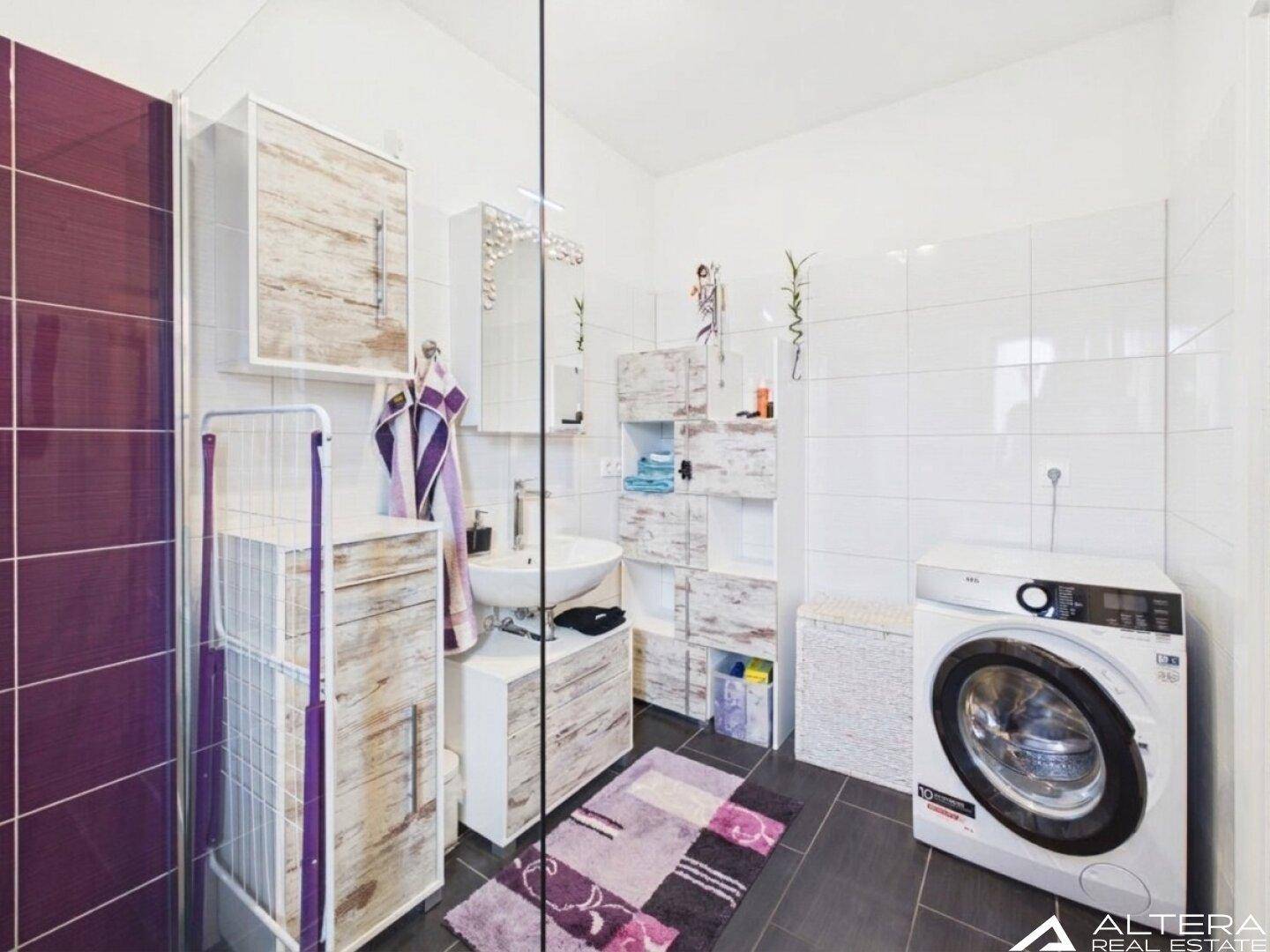 Geräumiges Badezimmer mit Waschmaschine, ebenerdiger Dusche und viel Stauraum, praktisch und hell.