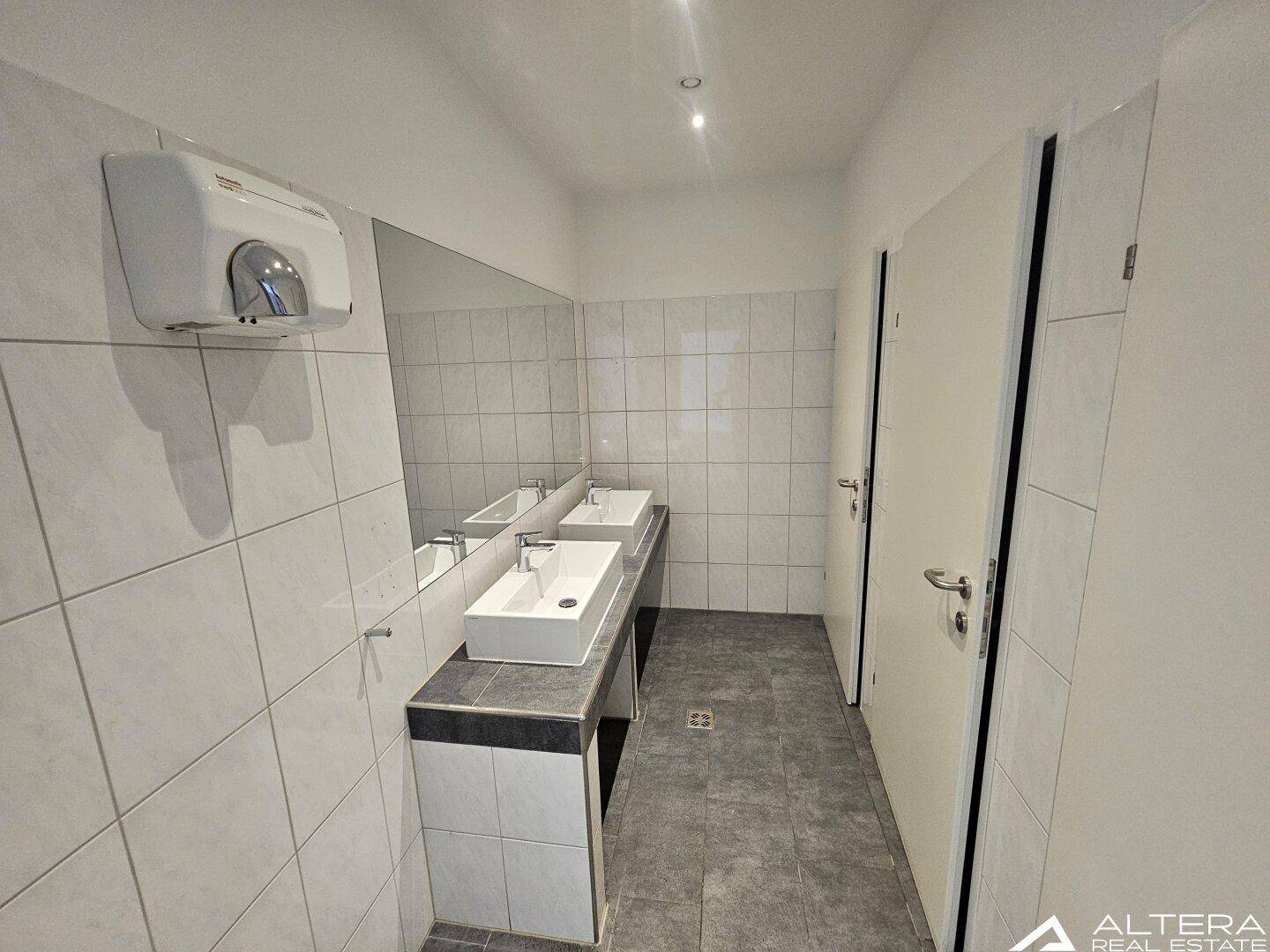 Moderner Waschraum mit zwei Aufsatzwaschbecken, großem Spiegel und Fliesen an Wänden und Boden.