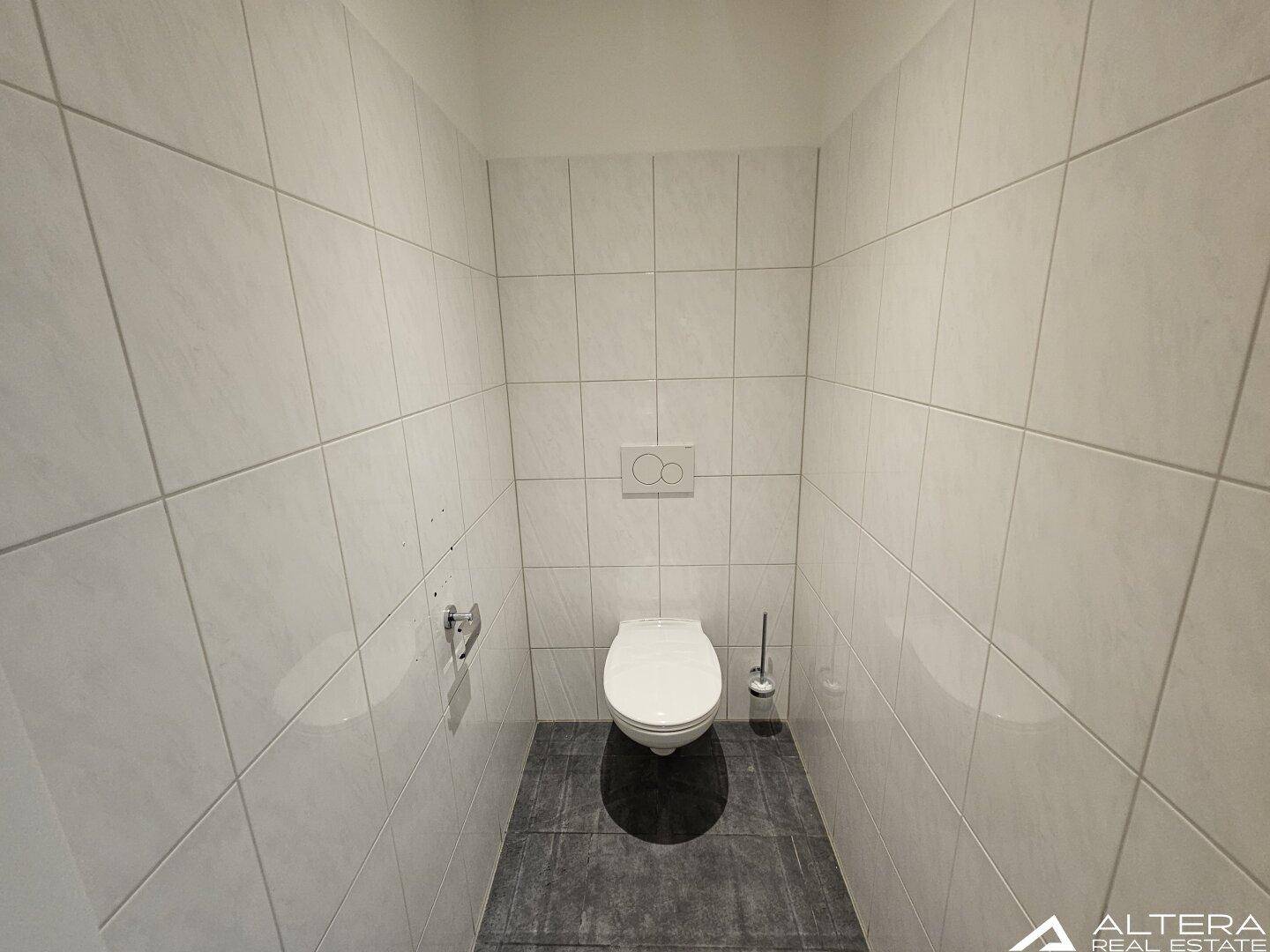 Einfache und saubere Toilettenkabine mit wandhängendem WC und vollständig gefliesten Wänden und Boden.