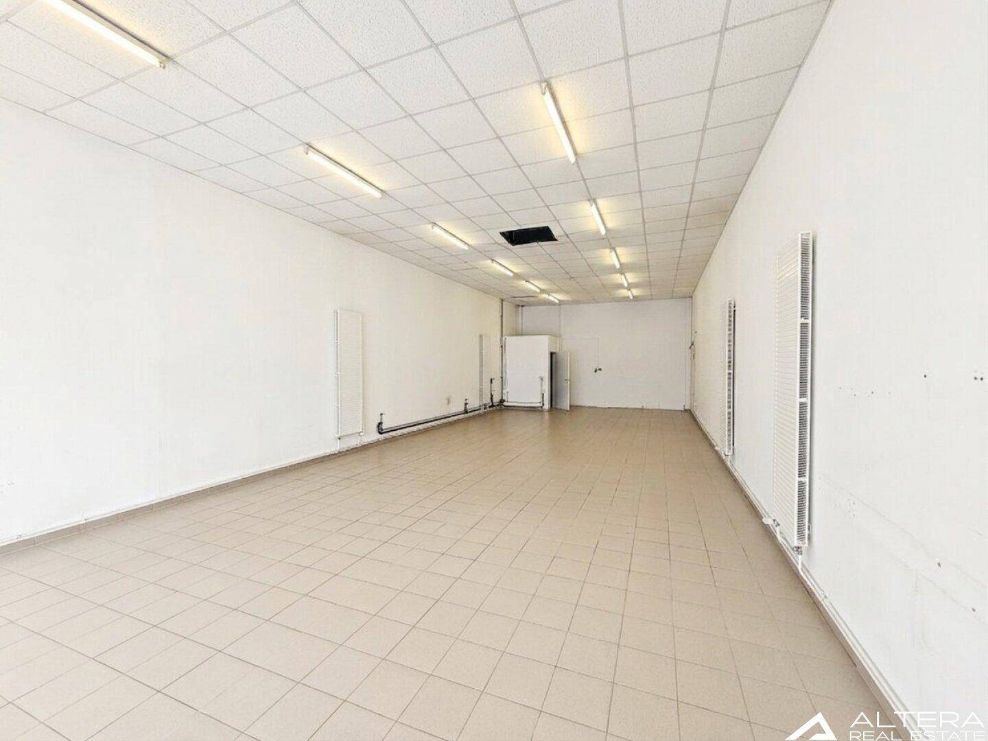 Heller, leerer Gewerberaum mit Fliesenboden und abgehängter Decke, bereit zur individuellen Gestaltung.