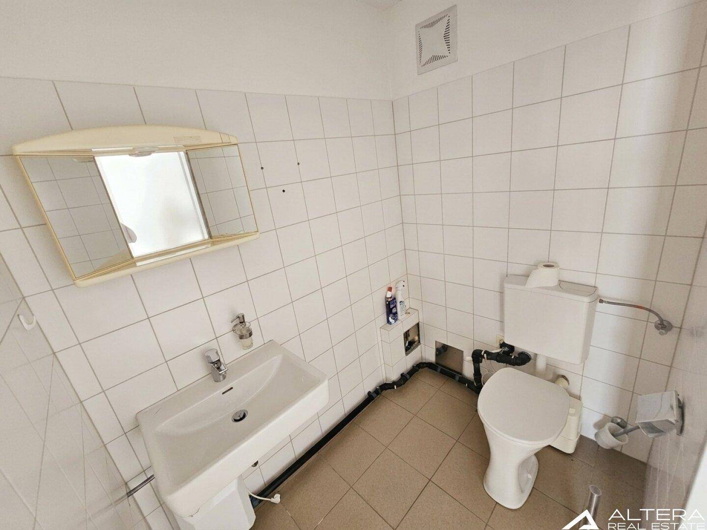 Kleines Badezimmer mit weißen Wandfliesen, WC, Waschbecken und Spiegelschrank.