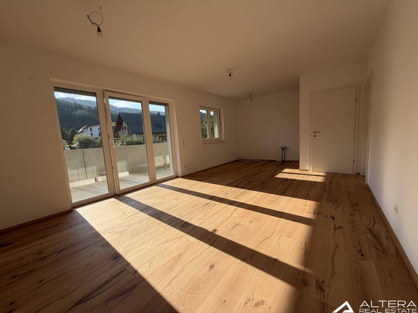 Helles Wohnzimmer mit Holzboden und Zugang zu einem Balkon, durchflutet von Sonnenlicht.