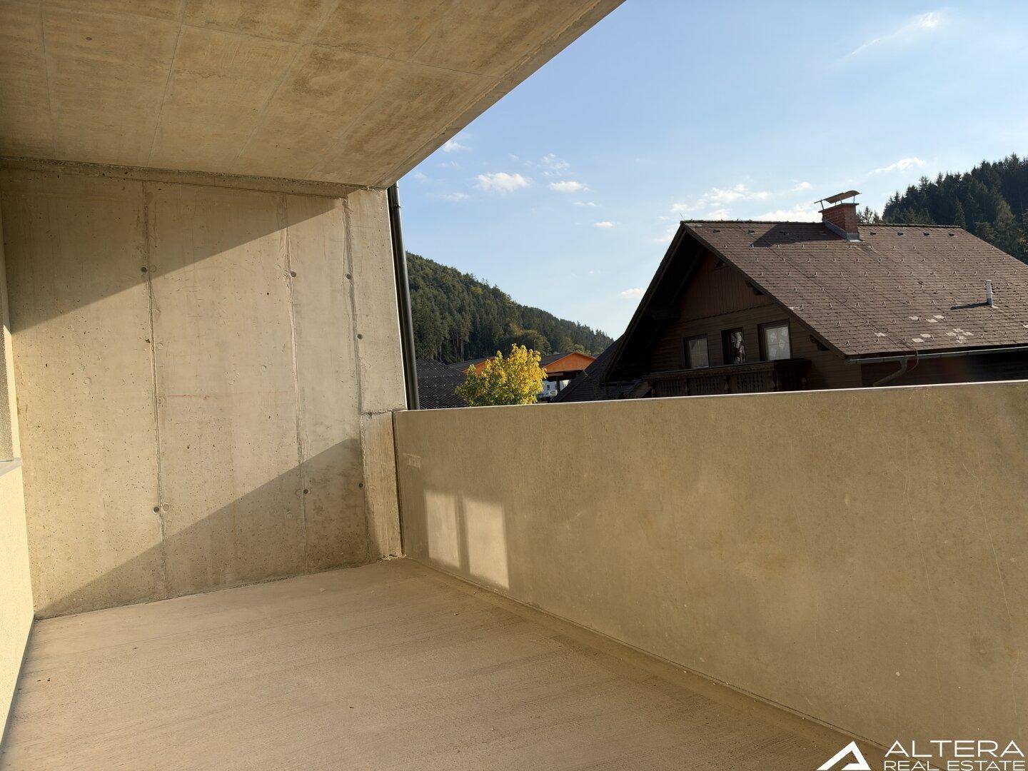 Balkon mit Betonboden und weitem Blick auf die grüne Umgebung und Berge.