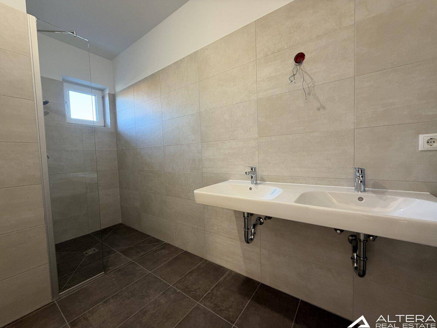 Modernes Badezimmer mit Doppelwaschbecken, begehbarer Dusche und hellen Fliesen.