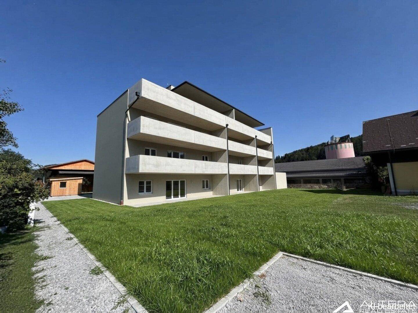 Seitenansicht eines neuen Mehrfamilienhauses mit Balkonen und weitläufiger Rasenfläche.