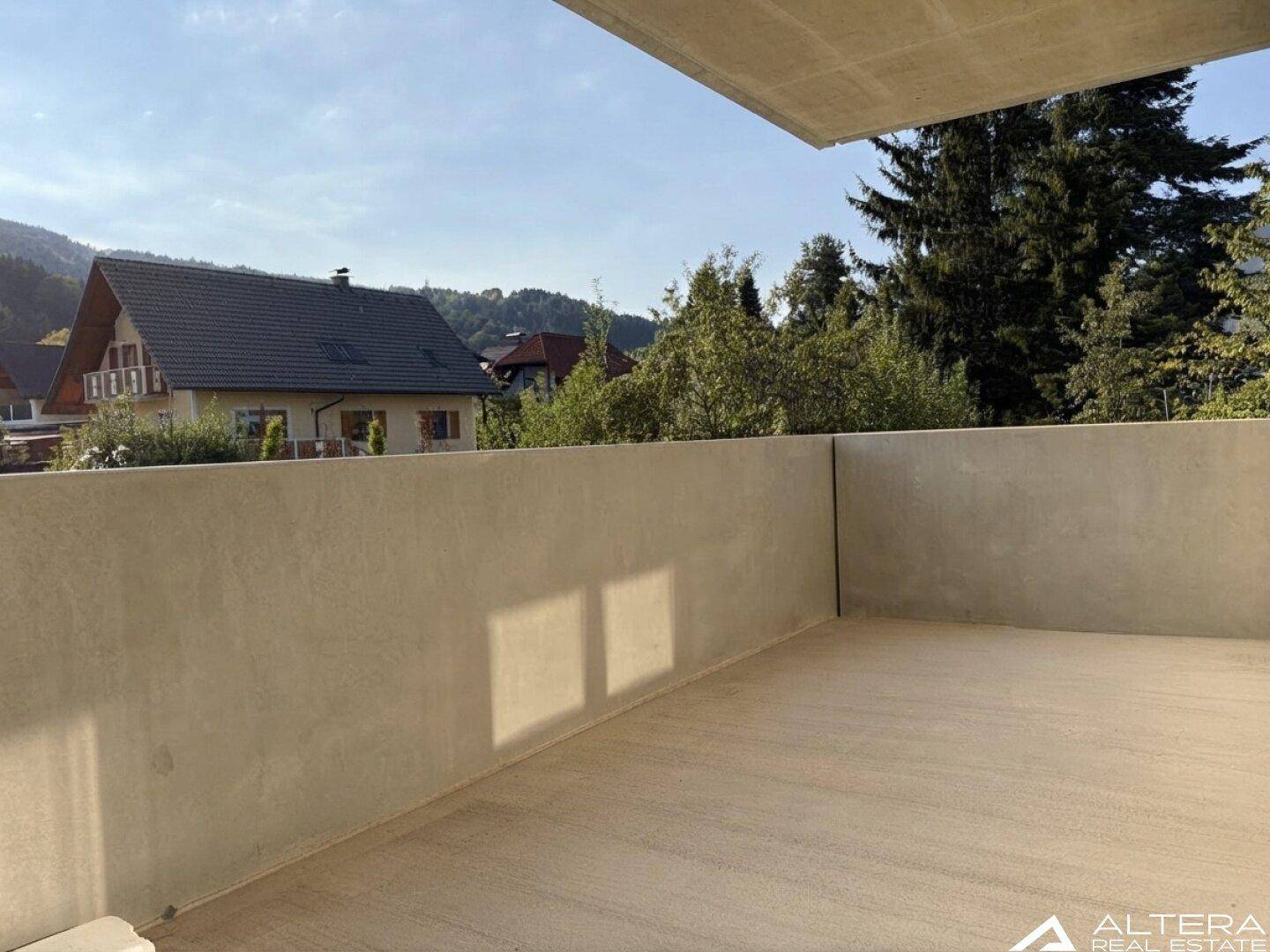 Geräumiger Balkon mit Betonboden und weitem Blick auf die umliegende Natur und Wohnhäuser.